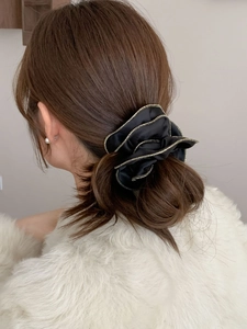 Gros plan d'un chouchou en satin noir avec bordure dorée sur un chignon élégant
