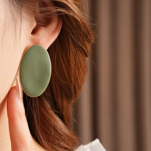 Dettaglio di un grande orecchino ovale verde opaco con bordo dorato su modella