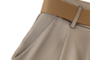 Detailed view of taupe satin trousers with brown leather belt and precise stitching