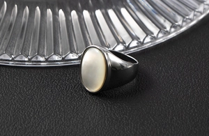Dettaglio macro di intarsio in conchiglia ovale su anello in acciaio scuro