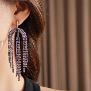 Detail of geometric tassel earrings with purple crystals and blue gemstone on model