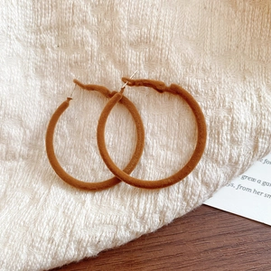 Detailed view of brown flocked velvet hoop earrings on a textured cream knit background