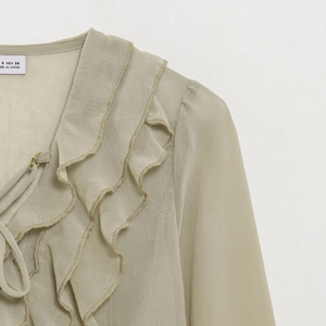 Detail of layered ruffle neckline and tie design on a sheer light green chiffon shirt