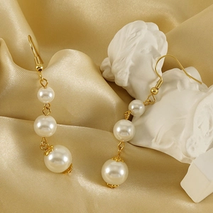 Détail de boucles d'oreilles en or 18 carats avec trois perles dégradées sur satin doré