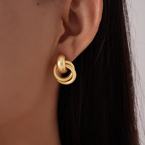 Détail macro de boucles d'oreilles nœuds multi-anneaux or mat portées par un modèle