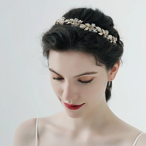Détail d'un serre-tête de mariée doré avec feuilles, perles et strass sur la coiffure