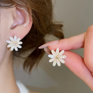 Close-up of white daisy stud earrings with glitter petals and a yellow diamond center