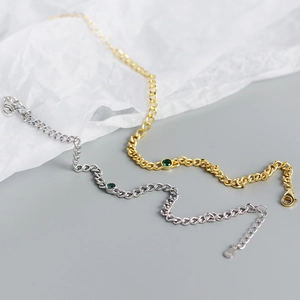 Close-up of gold and silver chunky chain bracelets with round green gemstones