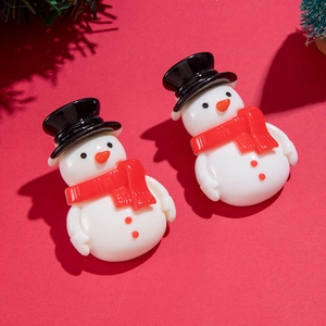 Gros plan d'adorables boucles d'oreilles bonhomme de neige en résine sur fond rouge