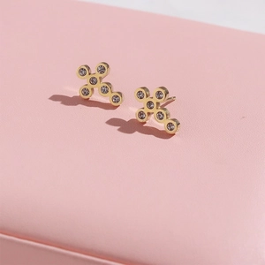 Elegant gold cross-shaped stud earrings with sparkling crystals on a pink jewelry box