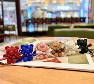 Detailed view of six colorful knitted bear keychains with ribbon bows on a magazine
