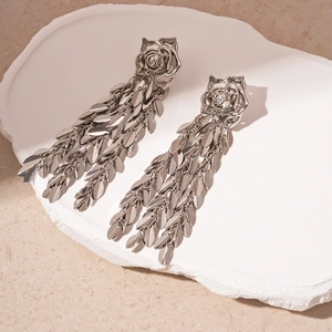 Macro detail of silver rose stud earrings with long metal leaf tassel on stone tray