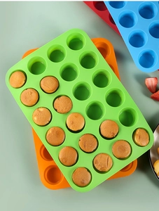Colorful 24-cavity silicone muffin molds with baked cupcakes on a light green countertop