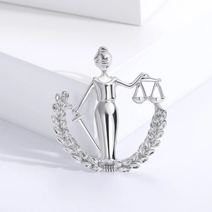 Macro shot of silver Lady Justice brooch featuring scales and sword on a white pedestal