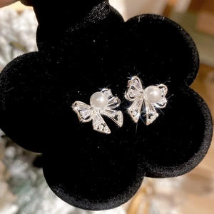 Macro shot of silver bow pearl stud earrings with sparkling pavé crystals on black velvet