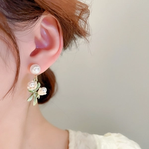 Gros plan de boucles d'oreilles muguet blanc avec feuilles vertes et perles dorées