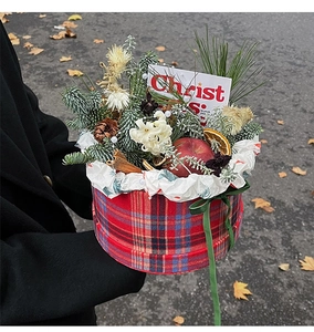 Detail of Christmas gift box featuring red plaid pattern, pine branch, apple and festive card