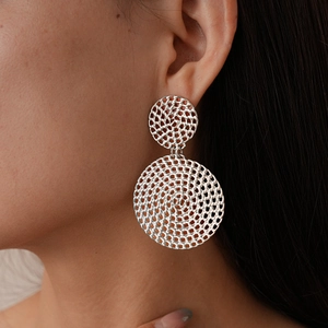 Gros plan de boucles d'oreilles géométriques en maille argentée portées par un mannequin