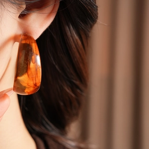 Close-up of amber resin C-shaped hoop earrings on a model showing marble texture