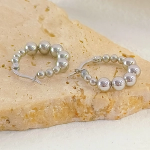 Macro shot of silver hoops with gradient metal spheres on a textured stone base