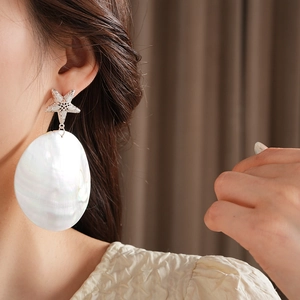 Close-up of oversized starfish silver earrings with large round white shell pendants