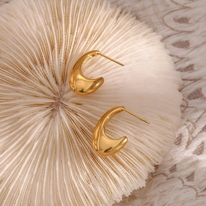 Macro view of gold-plated wide C-shape earrings on a white textured background