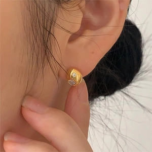 Close-up of gold ear studs featuring minimalist organic curves and zircon stones