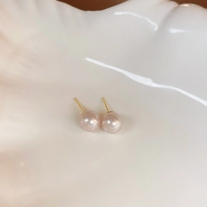 Macro shot of elegant round pearl stud earrings with gold posts on a textured tray