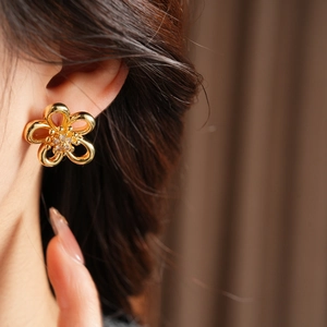 Detail view of a hollow golden flower earring with zircons worn on a model's ear