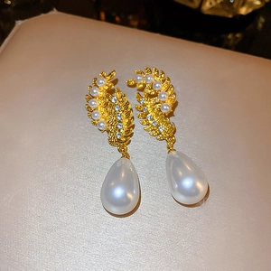 Macro detail of vintage gold feather earrings with sparkling crystals and drop pearls