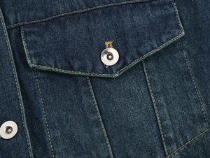 Détail macro d'une veste en jean indigo foncé montrant les coutures et le bouton métallique