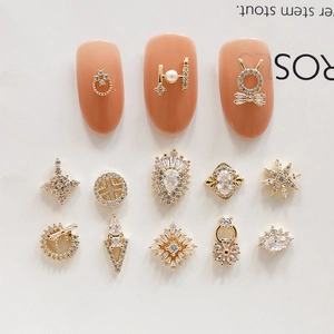 Ciondoli geometrici dorati per nail art con zirconi e perle su sfondo minimalista