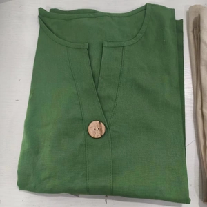 Dettaglio scollo a V con un bottone tondo in legno su un top verde in misto lino