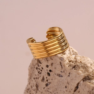 Gros plan sur bague dorée multi-rangs striée posée sur une base en pierre texturée