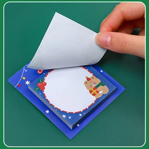 Dettaglio di una mano che stacca un post-it natalizio con orsetto da una base blu decorata