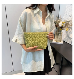 Close-up of grass green quilted floral clutch bag held by a model in a lifestyle setting