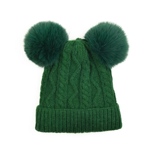 Détail du bonnet en tricot vert foncé avec deux pompons doux et maille torsadée
