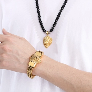 Close-up of golden lion head necklace with black beads and woven bracelet on model