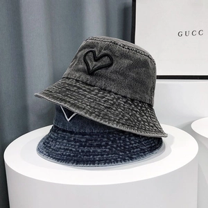 Close-up of heart embroidery on stacked washed denim bucket hats in gray and blue