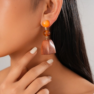 Detail view of bohemian drop earring with orange bead and wooden trapezoid pendant