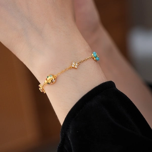 Close-up of golden charm bracelet with ladybug and turquoise clover on woman wrist