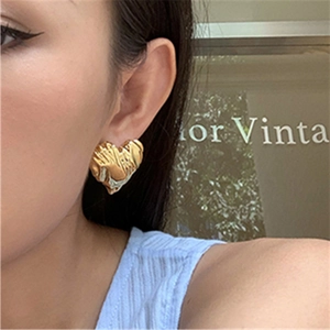 Detail shot of golden heart earrings with unique crinkled texture on a female model