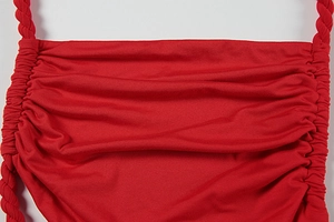 Detail of red knitted dress featuring lateral ruching and twisted rope shoulder straps