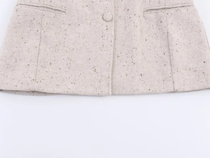 Détail de l'ourlet en tweed beige avec coutures fines et bouton en tissu assorti