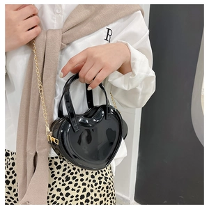 Detail view of heart-shaped black patent leather bag with a gold chain strap