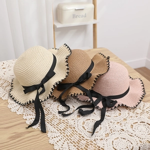 Bow straw sun hats in beige brown and pink with wavy black trim on a wooden table
