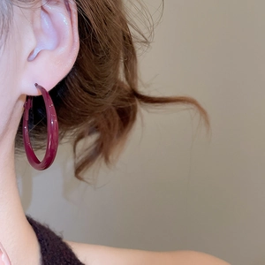 Close-up detail of large deep red glossy geometric hoop earrings worn by a model
