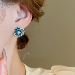 Close-up of a blue enamel flower earring with pearl center and crystals on ear lobe