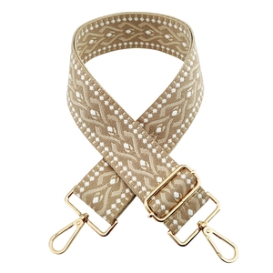 Detail of beige 5cm wide jacquard bag strap with white geometric patterns and gold buckles