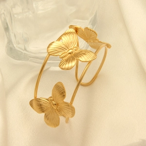 Polished gold butterfly open cuff bracelet displayed on soft white fabric background